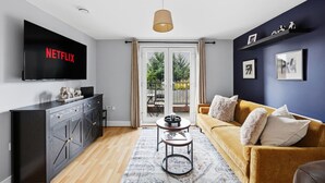 En moderne stue med et fladskærms-tv, en sofa, et sofabord og udsigt til det fri via en skydedør.