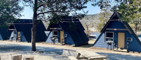 Una hilera de cabañas triangulares con mesas de picnic y fogones en un camping.