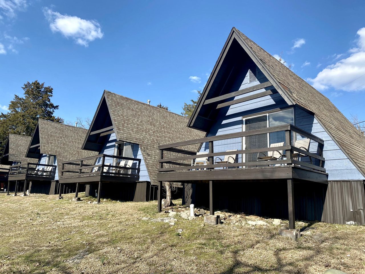 Une rangée de chalets modernes, dotés de toits inclinés et de balcons, s’étend sur une zone herbeuse sous un ciel dégagé.