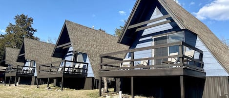 A row of modern cabins with sloped roofs and balconies, set in a grassy area with clear skies.