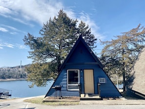 A small, triangular cabin by a lake with a door and a window. - Lovely A-Frame Cabin Rental with Amazing Lake Views in Branson, Missouri (Branson)