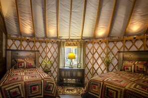 A yurt with two beds, a window with a lamp, and a small table with a plant.