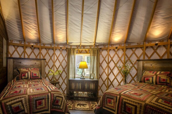 A yurt with two beds, a window with a lamp, and a small table with a plant.