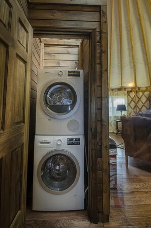 A compact laundry room with two stacked washing machines, wooden walls, and a visible window. - Group 07) Creekside Cove Yurt (Topton)