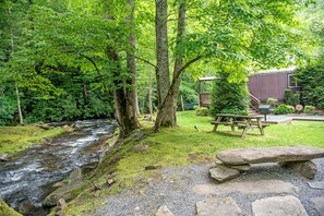 A natural outdoor setting with a stream, picnic table, and stone seating area. - Group 07) Creekside Cove Yurt (Topton)