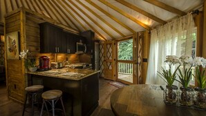 A rustic kitchen with wooden cabinets, a central island, bar stools, and a dining table with a vase of flowers. - Creekside Secluded Yurt with Jacuzzi in Topton, North Carolina (Topton)