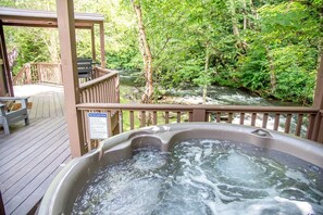 A hot tub on a wooden deck with a river view, a safety sign, and a bench. - Creekside Secluded Yurt with Jacuzzi in Topton, North Carolina (Topton)
