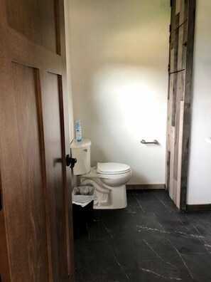 Une petite salle de bain propre, équipée de toilettes, d’une poubelle et d’un porte-rouleau de papier toilette.