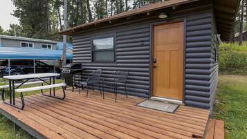 Eine Blockhütte mit einer Terrasse, einem Grill und einer Fußmatte.