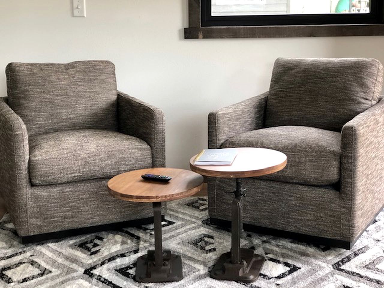 Two grey armchairs, a small round wooden table with a remote control, and a patterned rug.