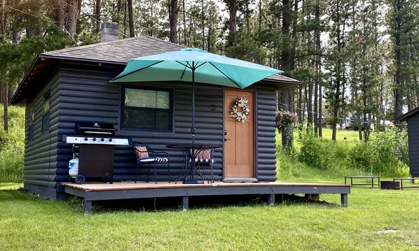 Una cabaña de troncos con una terraza, una parrilla al aire libre y una mesa con sillas.