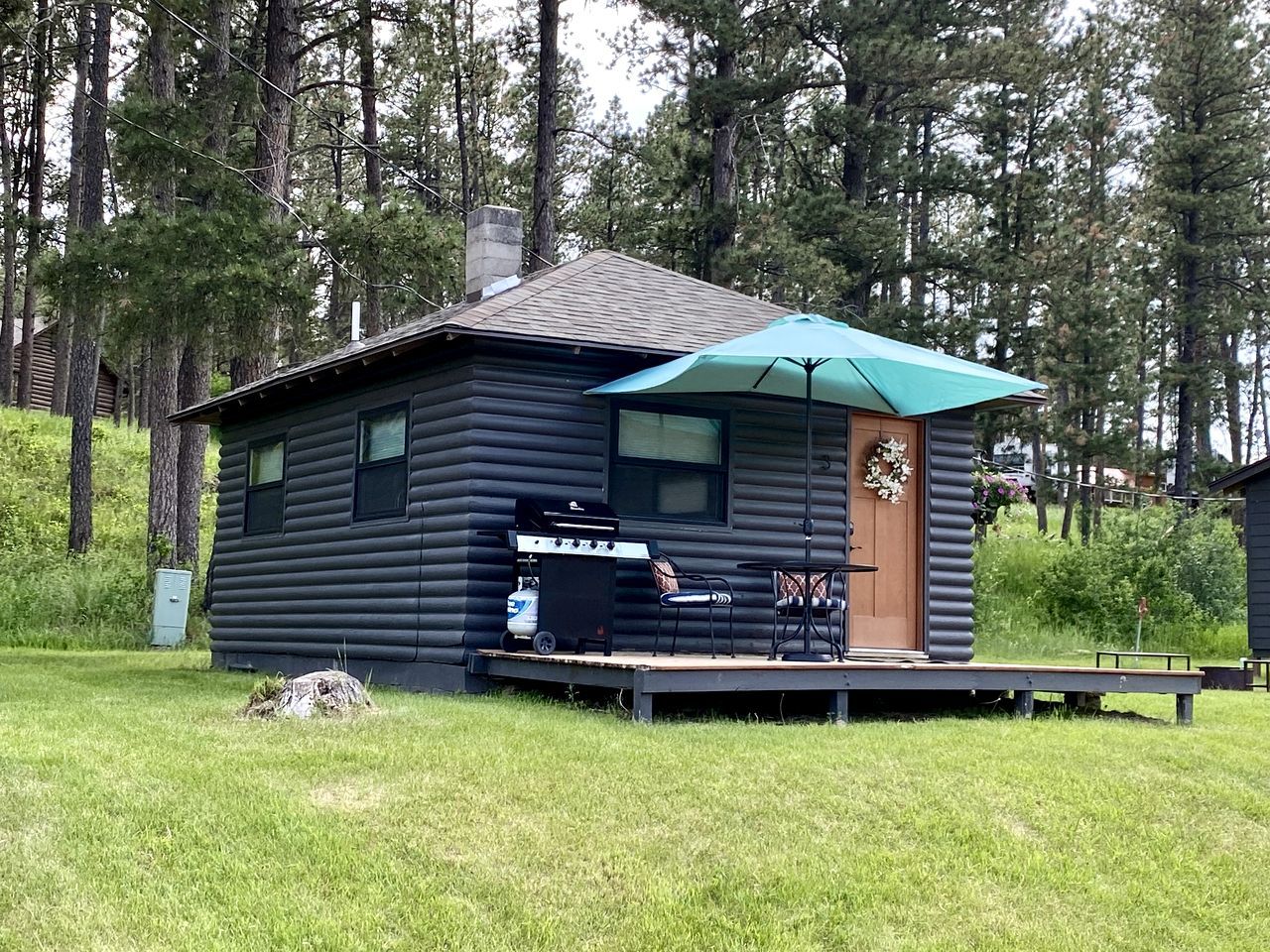 Une cabane en rondins dotée d’une terrasse, d’un barbecue extérieur et d’un grand parasol.