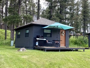 Una cabaña de troncos con terraza, parrilla exterior y un paraguas grande.