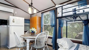 A compact room with a bunk bed, a small table with chairs, a refrigerator, and a window with curtains. - Picturesque Cabin with Fire Pit in Miami, Oklahoma (Miami)