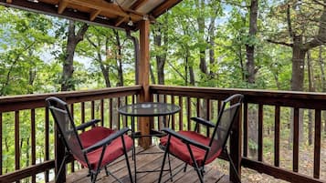 Een houten terras met een tafel en twee stoelen, omringd door een houten balustrade, met uitzicht op een bebost gebied.