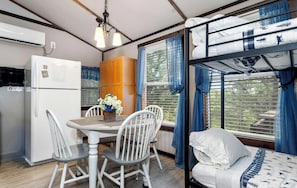 A compact room with a bunk bed, a small table with chairs, a refrigerator, and a window with curtains. - Picturesque Cabin with Fire Pit in Miami, Oklahoma (Miami)