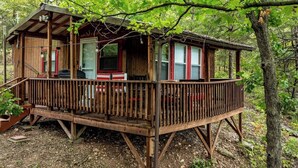 A wooden cabin with a deck, surrounded by trees.