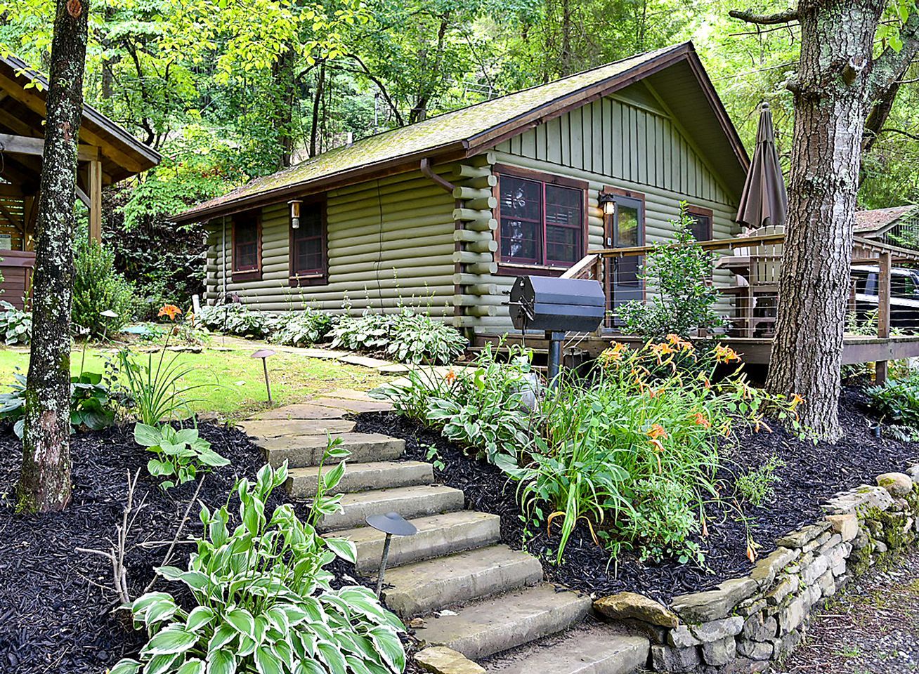A log cabin with a stone staircase leading to the entrance, surrounded by a garden with various plants and flowers.
