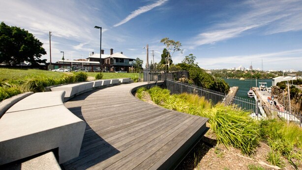 A curved wooden deck with a railing, overlooking a body of water and a cityscape. - Woolwich Studio Bliss, Private Oasis by the Water (Sydney)