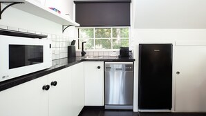 A modern kitchen with white cabinetry, a black countertop, a built-in microwave, a dishwasher, and a refrigerator. - Woolwich Studio Bliss, Private Oasis by the Water (Sydney)