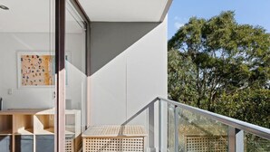Un balcon moderne avec une balustrade en verre, un banc en bois et une vue sur les arbres.