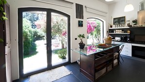 Una cocina moderna con una isla de vidrio, un comedor con una silla y grandes puertas correderas de vidrio que dan a un jardín.