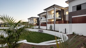 A modern residential building with multiple balconies, a well-maintained lawn, and a curved driveway. - 3-bed Apartment in Beautiful Kiama With Study Nook (Kiama)