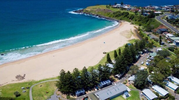 An aerial view of a coastal area with a beach, houses, and a road. - 3-bed Apartment in Beautiful Kiama With Study Nook (Kiama)