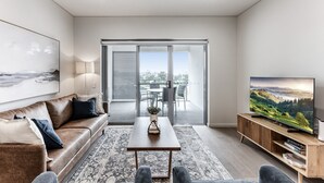 A modern living room with a sofa, coffee table, and TV. - 3-bed Apartment in Beautiful Kiama With Study Nook (Kiama)