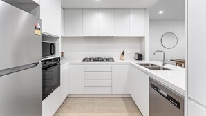 A modern kitchen with white cabinets, a built-in oven, a microwave, a gas stove, and a dishwasher. - 3-bed Apartment in Beautiful Kiama With Study Nook (Kiama)