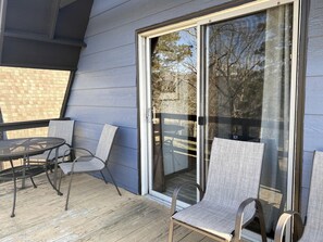 Eine überdachte Terrasse mit Tisch und Stühlen, eine Glasschiebetür und Blick auf ein Backsteinhaus.