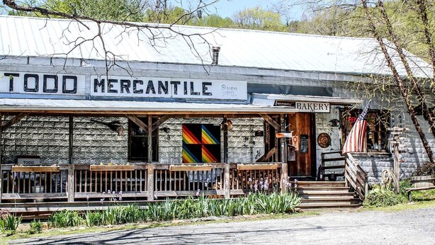 Um edifício rústico com uma placa que diz 'TODD MERCANTILE' e uma placa 'PADARIA' acima da entrada.