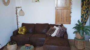 Ein Wohnzimmer mit einem braunen Ecksofa, einer Wanduhr, einer Holztür und einem Blumentopf.