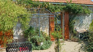 Ein rustikales Steinhaus mit Ziegeldach, einer Holztür und einem Kieshof mit Blumentöpfen und Gartenmöbeln.