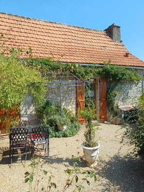 Ein rustikales Steinhaus mit Ziegeldach, einer Holztür und einem Kieshof mit Blumentöpfen und Gartenmöbeln.
