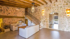 A spacious living area with a stone wall, a white sofa, a wooden coffee table, a staircase, and a stone archway leading to another room. - Country House 'Sunshine' with Mountain View, Wi-Fi and Air Conditioning (Sant Joan)