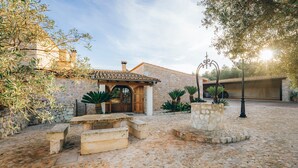 A courtyard with a stone building, a wooden door, and a stone bench. - Country House 'Sunshine' with Mountain View, Wi-Fi and Air Conditioning (Sant Joan)