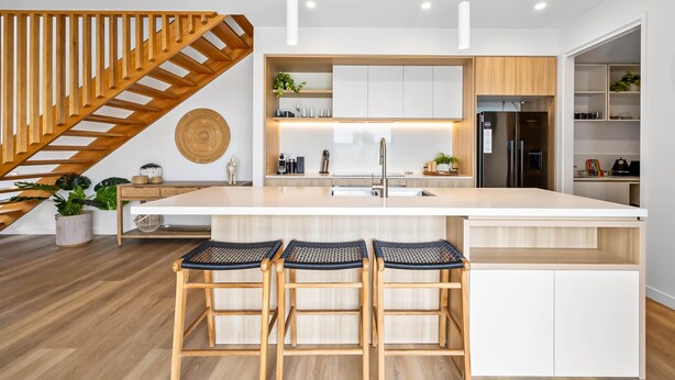 A modern kitchen with a central island, wooden bar stools, and a staircase. - Bokarina 3-bed Stunning Home, Steps From Beach (Sunshine Coast)