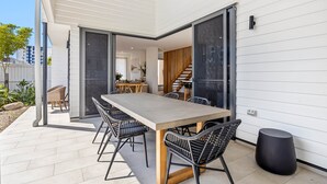 A modern outdoor patio with a long table and chairs, a wooden bench, and a black stool. - Bokarina 3-bed Stunning Home, Steps From Beach (Sunshine Coast)