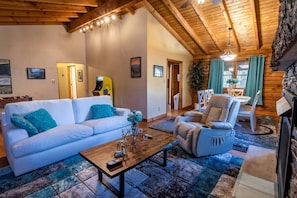 A cozy living room with a sofa, armchair, coffee table, and fireplace. - Glamping Retreat near Summersville Lake: Luxurious Cabin with a Hot Tub in Mt Nebo, WV (Mount Nebo)