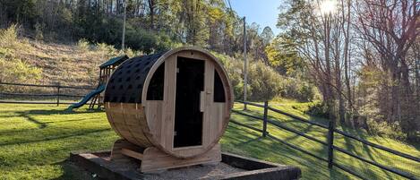 Uma estrutura em madeira com porta, cercada por um gramado e uma cerca de madeira.