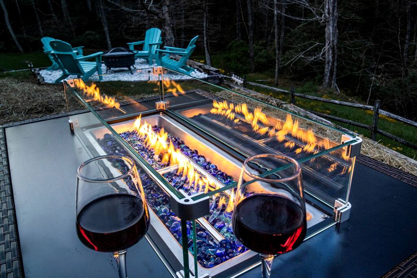 An outdoor fire feature with two glasses of red wine on a table.