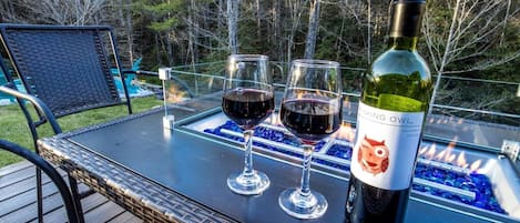 A bottle of wine and two glasses on an outdoor table with a view of trees.