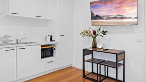 A modern kitchen with white cabinetry, a built-in oven, and a wooden dining table with a vase of flowers. - Stunning Studio Apartment Near Public Transport (Melbourne)