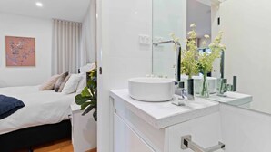 A modern bedroom with a large bed, a white bedside table, a round white sink, and a mirror above the sink. - Stunning Studio Apartment Near Public Transport (Melbourne)