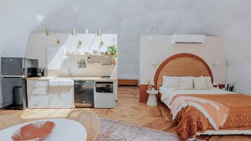 Een compacte, moderne kamer met kitchenette, een bed met houten hoofdeinde en een klein nachtkastje.
