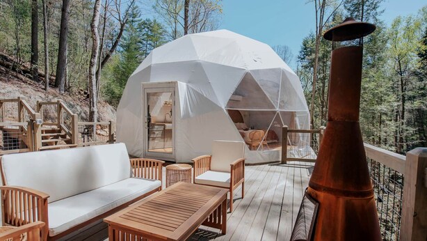Una estructura en forma de cúpula geodésica con terraza de madera, mobiliario exterior y chimenea.