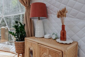 Una habitación con ventana, una lámpara, un reloj, un florero con plantas secas y una planta en maceta.