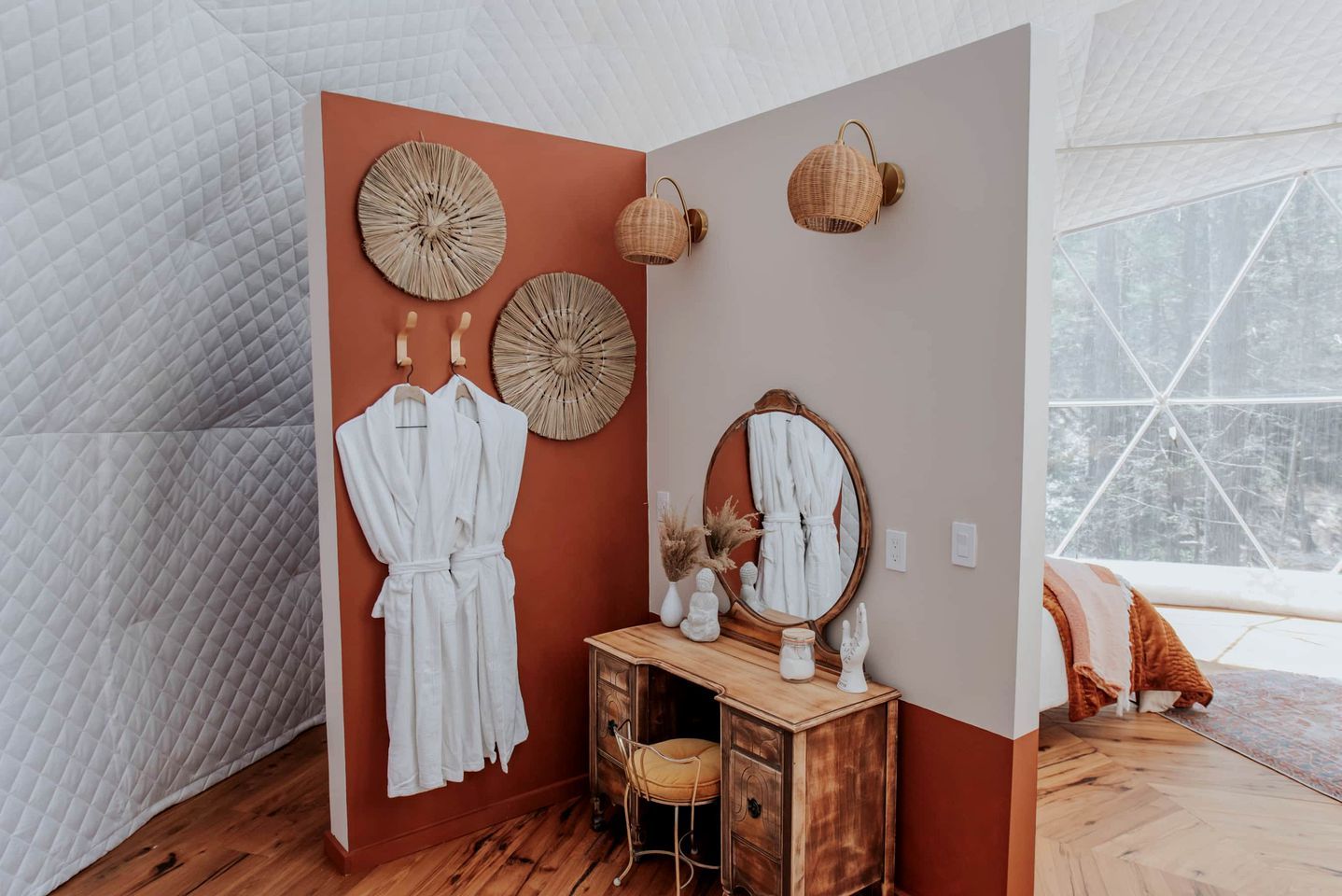 A room with a wooden dresser, a mirror, two hanging robes, and decorative wall art.