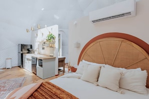 A compact bedroom with a bed, bedside table, and a kitchenette area.